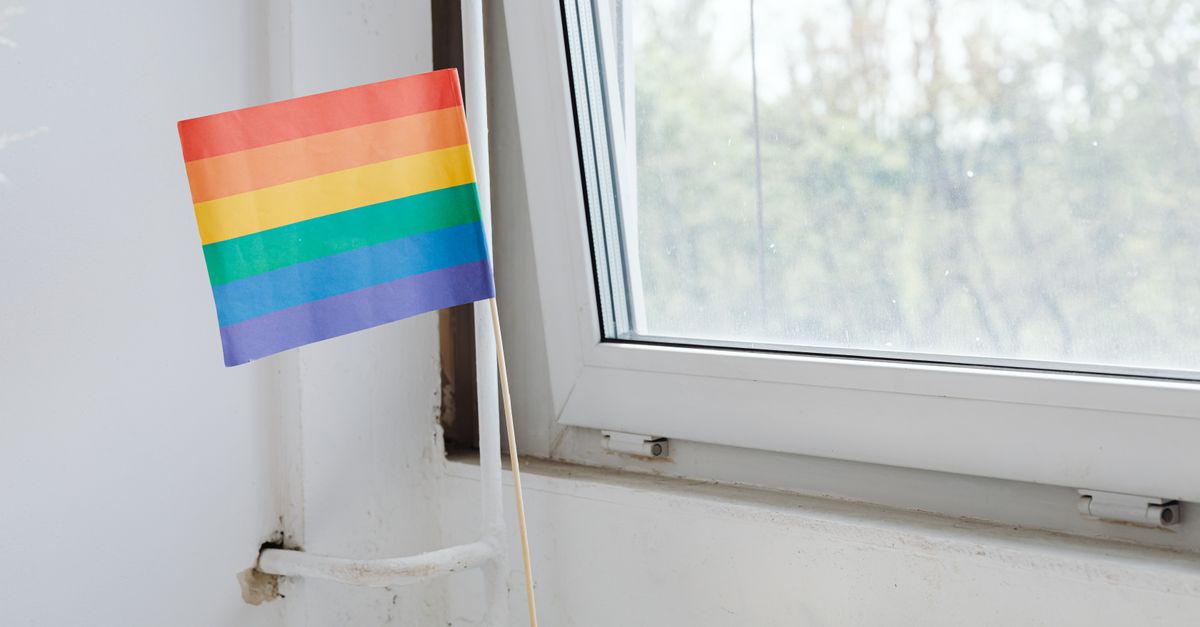 A vibrant rainbow flag displayed next to a window, symbolizing LGBTQ pride and inclusivity.
